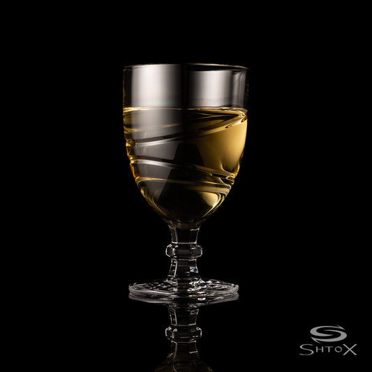 Crystal rotating wine glass with a sleek swirling design, filled with light golden liquid, set against a black background with the Shtox logo at the bottom.
