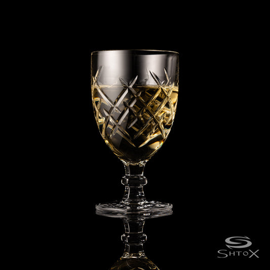 Elegant crystal rotating wine glass with intricate geometric pattern, filled with a light golden liquid, placed against a black background, featuring the Shtox logo at the bottom.