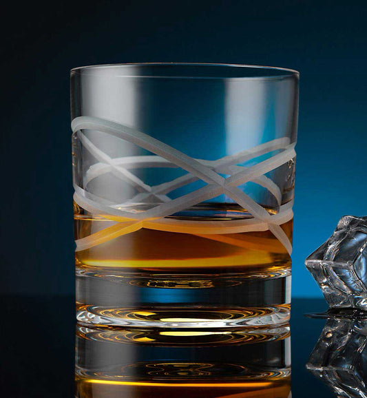Crystal whiskey rotating glass with amber liquid, featuring a modern geometric design and a reflective surface, alongside a faceted ice cube on a dark background.