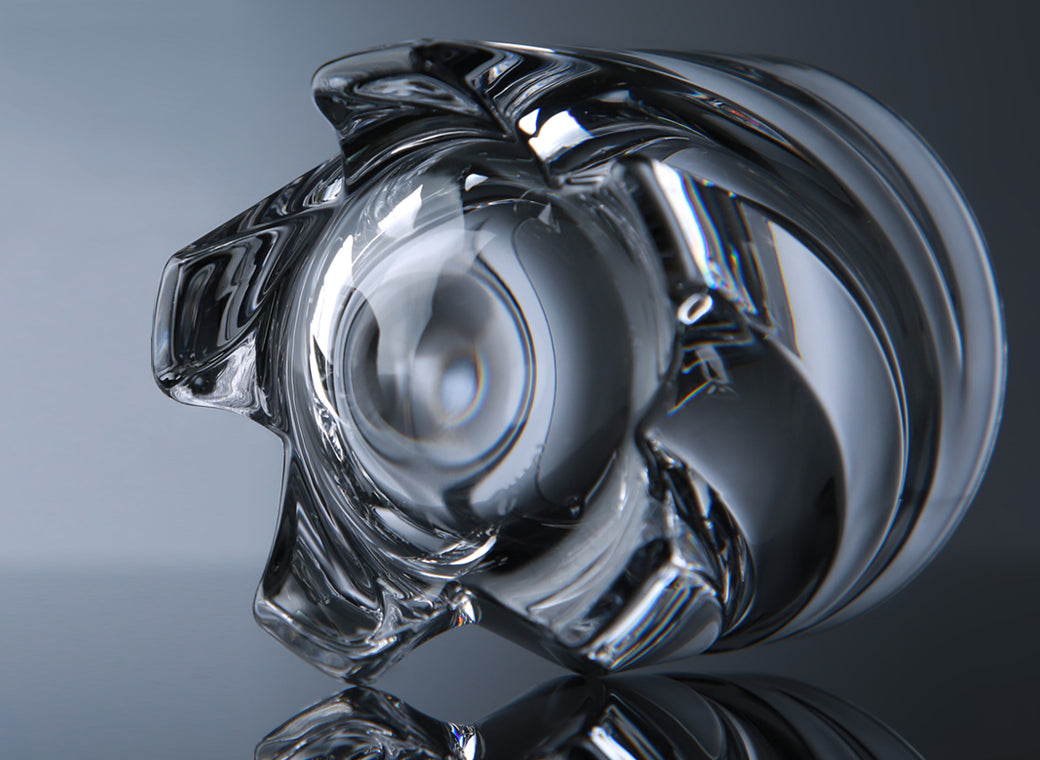 Close-up view of the bottom of a crystal shot glass with a unique, twisted design, placed on a reflective surface against a soft blue background.
